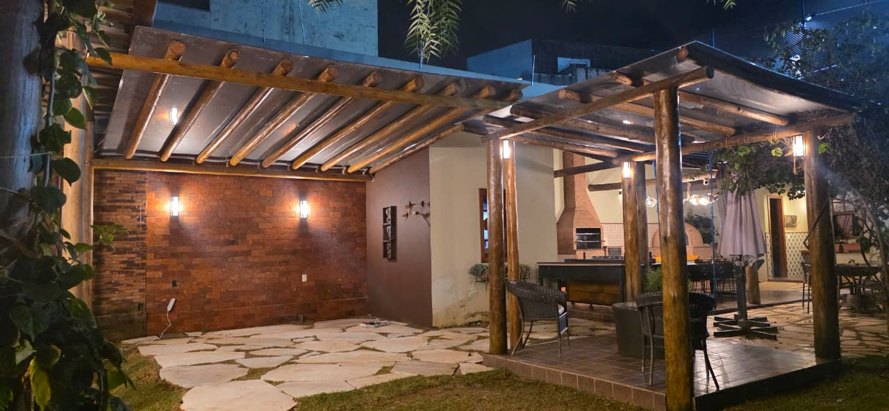 Deck sob o pergolado com as luminárias acesas ao anoitecer