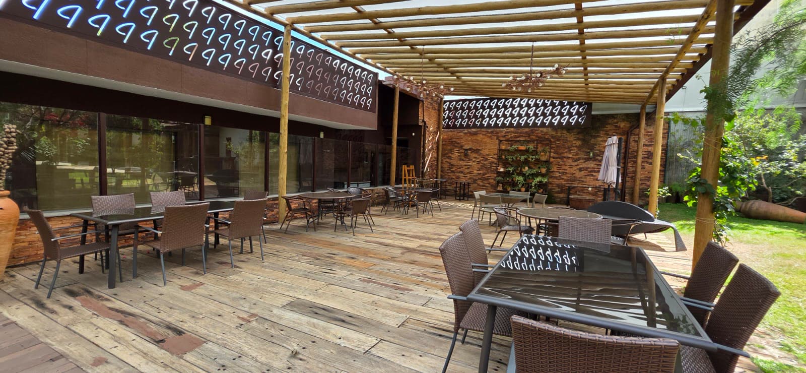Jardim com deck de madeira coberto por pergolado de eucalipto, mesas e cadeiras de fibra